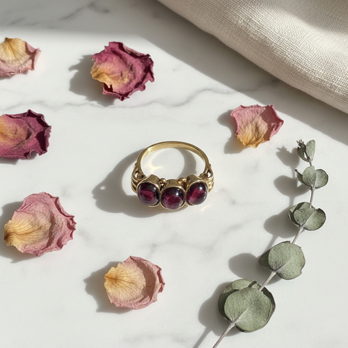 1880s antique gold garnet engagement ring with three cabochon stones, styled on marble with dried rose petals and eucalyptus